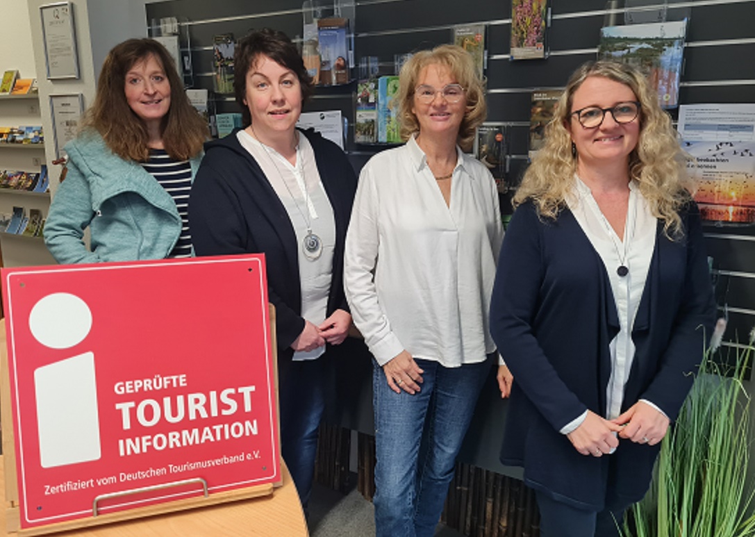 Team der Tourist Information Dümmer (TID) vor Infowand mit Prospekten und Zertifizierungsschild.