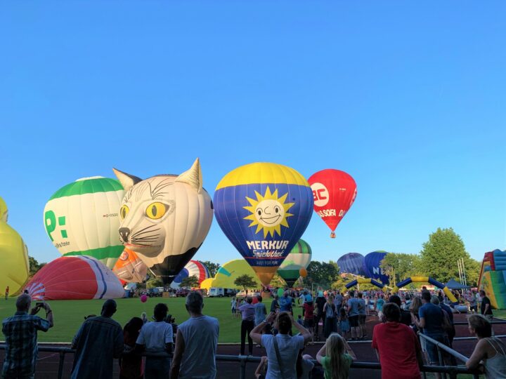 Heißluftballons beim Barnstorfer Ballonfahrer-Festival, darunter ein auffälliger Ballon in Katzenform und viele Besucher auf dem Festgelände.