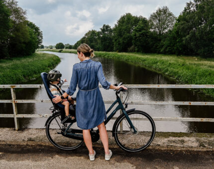Eine Frau steht auf einer Brücke mit einem Fahrrad, auf dem im Kindersitz ein Kleinkind sitzt.