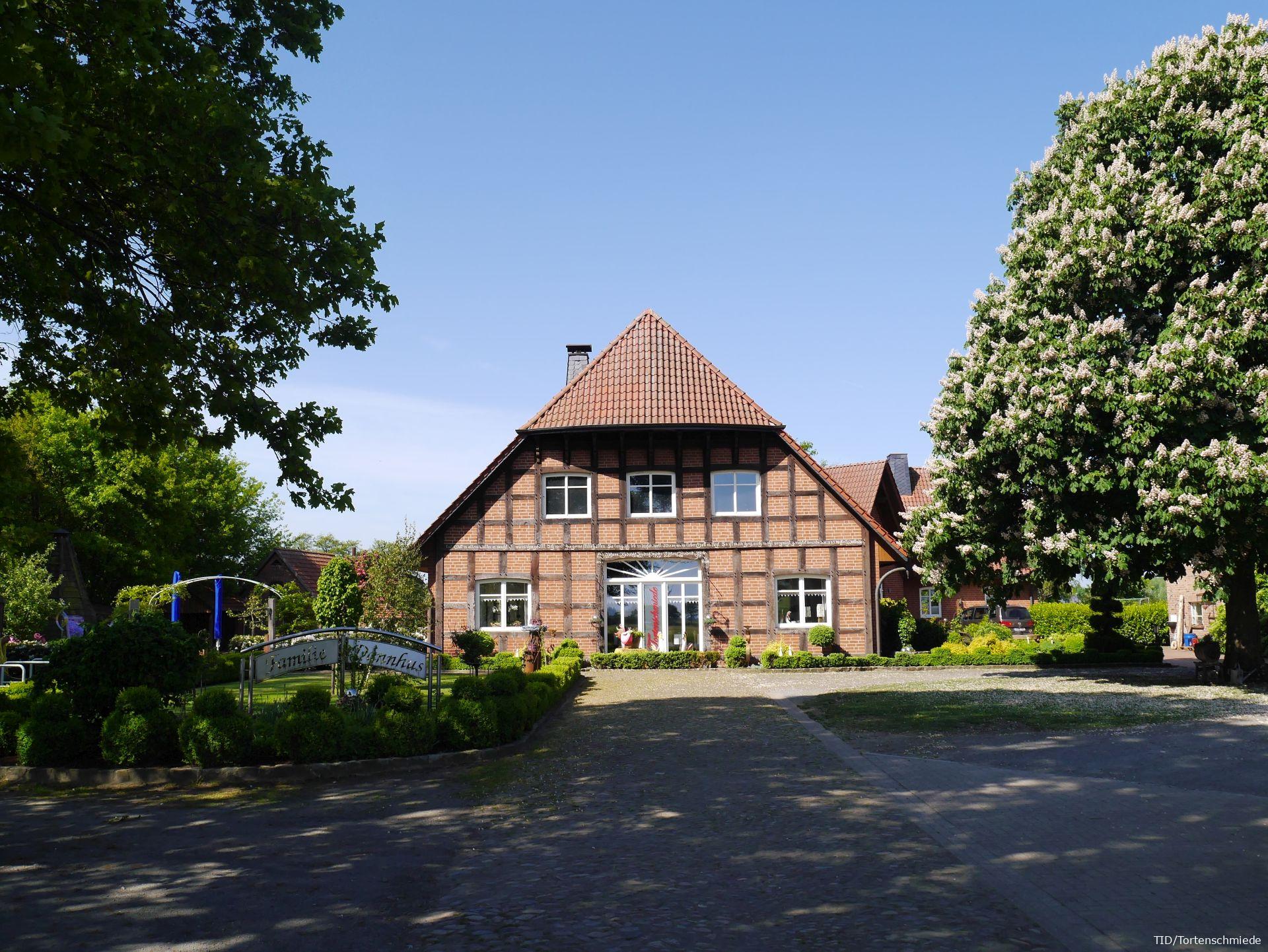 Das Fachwerkhaus der Tortenschmiede erstrahlt unter blauem Himmel, umgeben von blühenden Bäumen und liebevoll gepflegtem Grün.